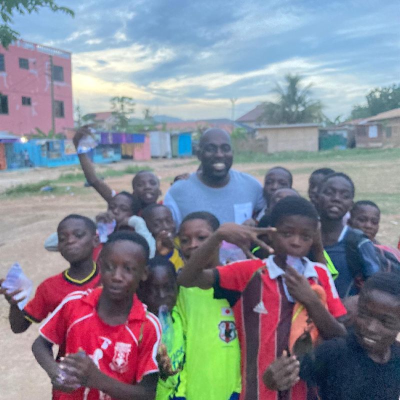 A coach laughing among a crowd of children holding sachets of drinking water